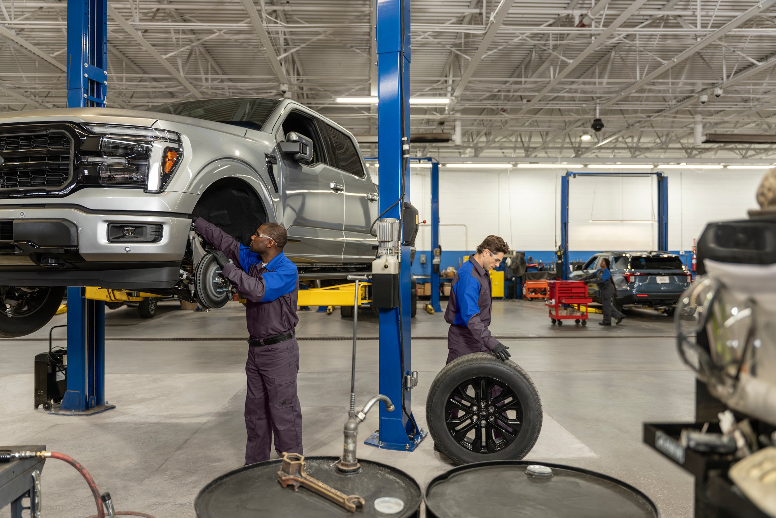 Ford service technicians working on an F-150 raised on a lift in a service bay