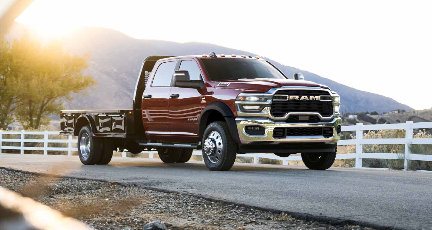 Red Ram Chassis Cab with a flatbed upfit parked by a white ranch fence