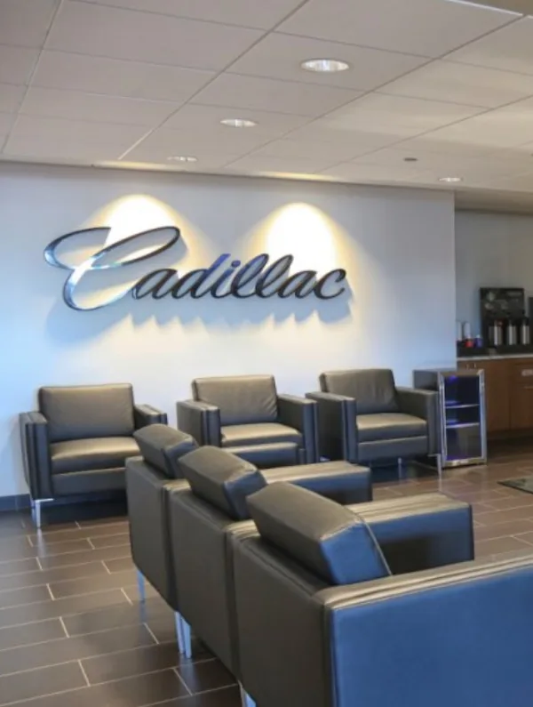 Customer lounge with leather chairs under a lit Cadillac wall script at Rizza Cadillac